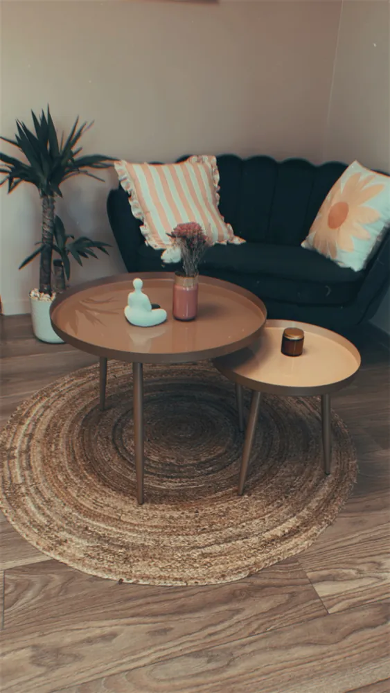 Le coin salon : canapé de velours vert, coussins rayés et fleuris, tables gigognes terracotta sur un tapis en jute.